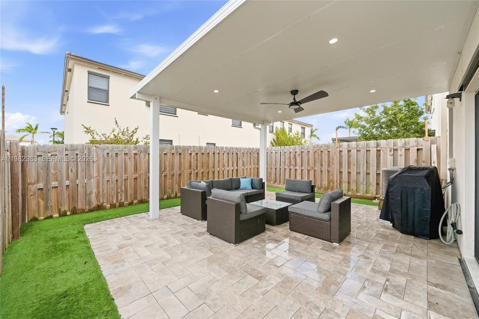 A paved patio with outdoor furniture sits under a covered roof in a fenced backyard — 13091 SW 232nd Ln, Miami FL 33170, MIAMI, FL
