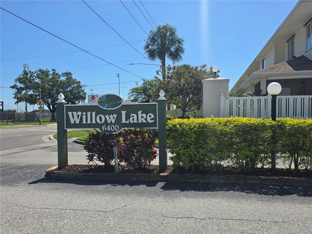 A green sign for Willow Lake stands near a road with a building behind it — 6400 46TH AVENUE N UNIT 301, KENNETH CITY, FL