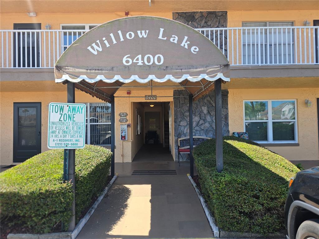 The exterior entrance of a multi-story apartment building features a tan facade and awning — 6400 46TH AVENUE N UNIT 301, KENNETH CITY, FL