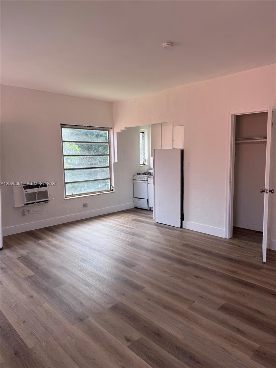 An unfurnished room features wood-look flooring, a window air conditioner, and an adjacent kitchen area — 825 Alton Road # 8, Miami Beach FL 33139, MIAMI BEACH, FL