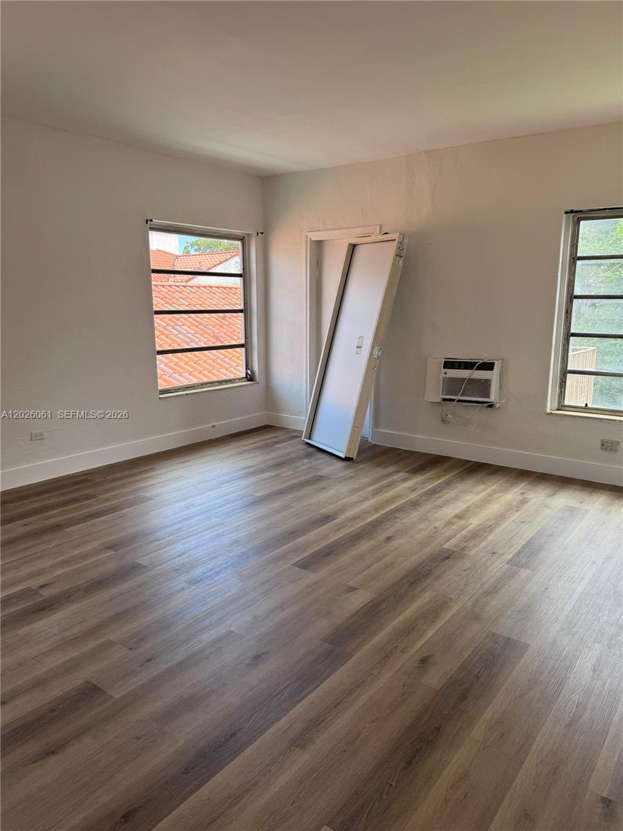 An empty room features wood-look flooring, white walls, two windows, and a detached door — 825 Alton Road # 8, Miami Beach FL 33139, MIAMI BEACH, FL