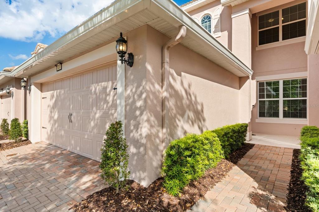 A beige house exterior features a two-car garage, a paved walkway, and manicured green shrubs — 1483 EL CONTE DRIVE, DAVENPORT, FL