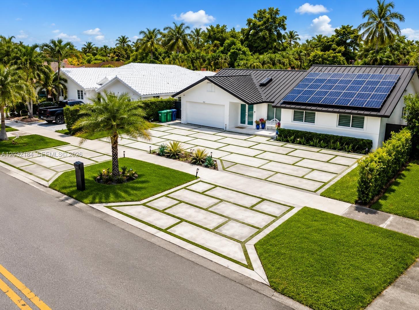 An exterior view of a white house with a metal roof, solar panels, and a paved driveway — 12440 SW 96th St, Miami FL 33186, MIAMI, FL