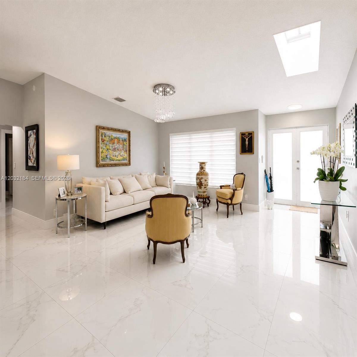 A bright living room features white marble floors, a beige sofa, and a crystal chandelier — 12440 SW 96th St, Miami FL 33186, MIAMI, FL