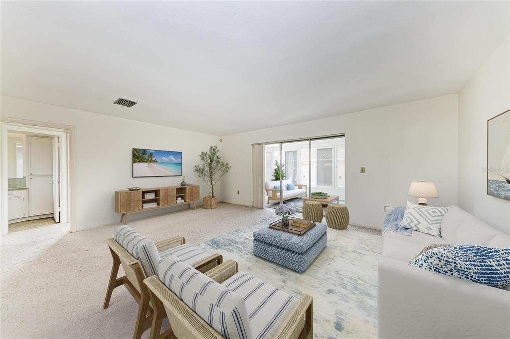 A living room with carpeted floors, a blue ottoman, and a sliding door to a patio — 507 GULF STREET, VENICE, FL