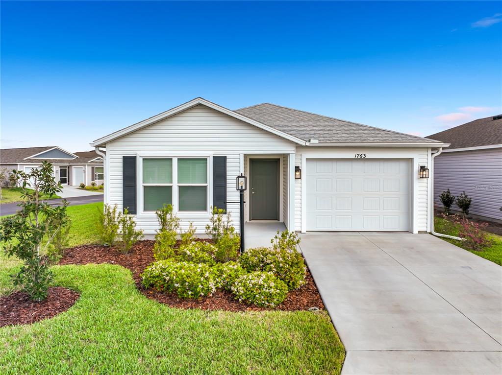 A single-story house with white siding, a front-facing garage, and a landscaped front yard — 1763 BRODY COURT, THE VILLAGES, FL