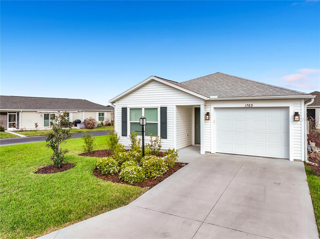 A single-story house with white siding, a one-car garage, and a landscaped front yard — 1763 BRODY COURT, THE VILLAGES, FL