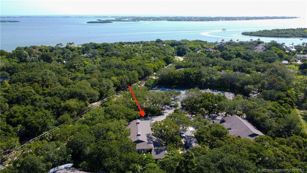 An aerial view shows a residential building nestled within a dense forest near the water — 5300 SE Schooner Oaks Way, Stuart FL 34997, STUART, FL