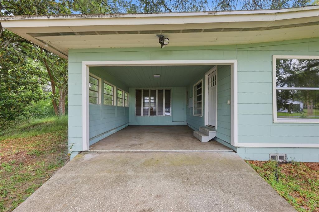 An open-air carport with light green siding, concrete flooring, and a white entry door — 1881 COTTONWOOD STREET, ORANGE CITY, FL