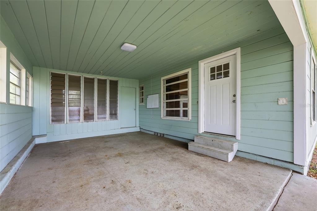 A covered concrete patio features light green horizontal siding and a white entry door — 1881 COTTONWOOD STREET, ORANGE CITY, FL