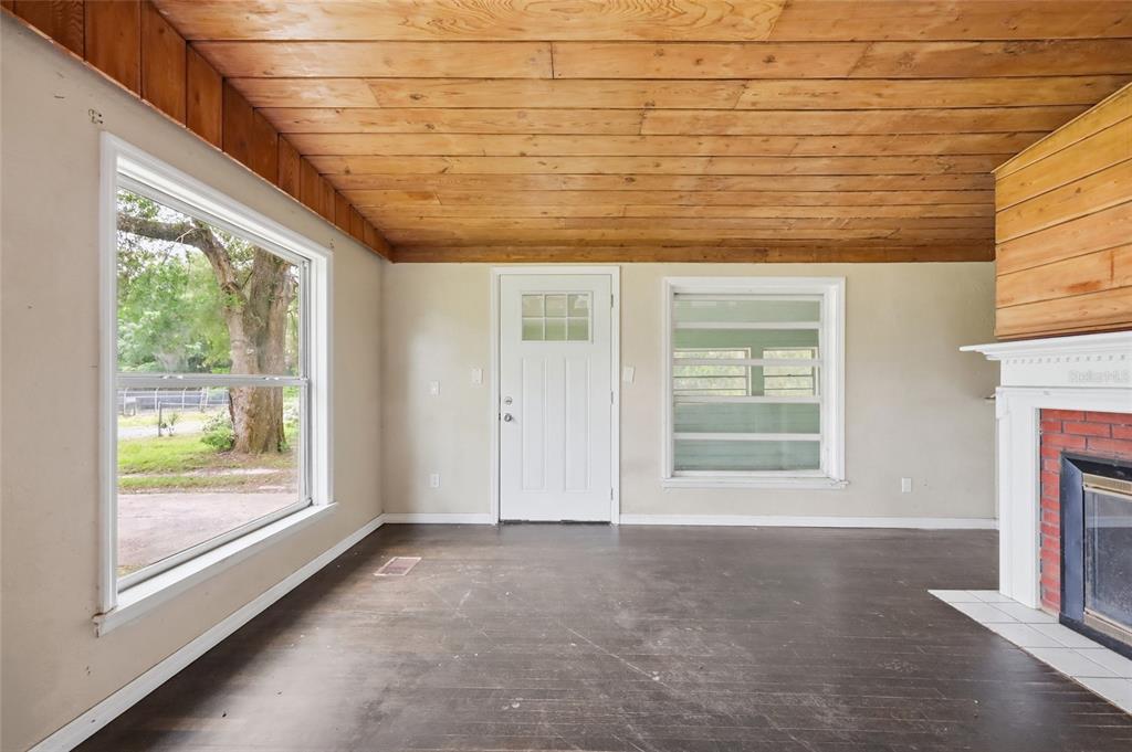 A room with a wood-plank ceiling, dark flooring, a fireplace, and a white exterior door — 1881 COTTONWOOD STREET, ORANGE CITY, FL