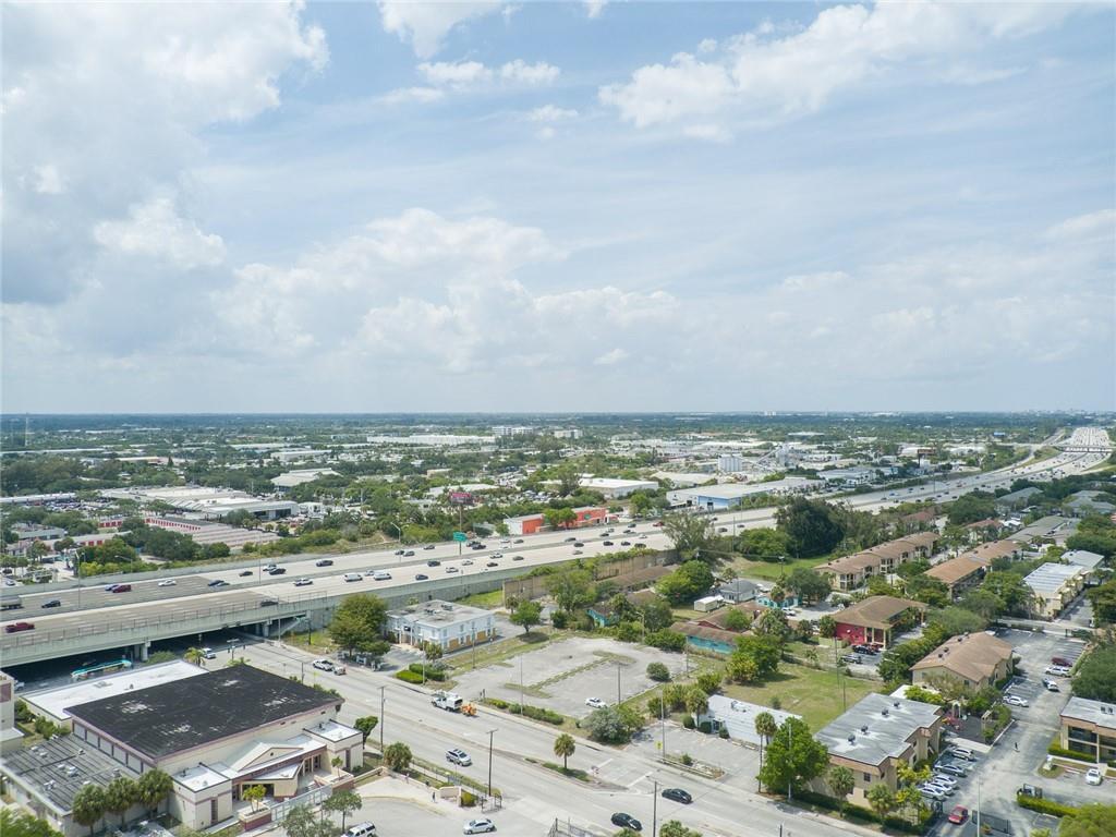 An aerial view shows a highway overpass, surrounding commercial buildings, and parking lots under a cloudy sky — 1744 Lake Worth Road, FL 33460, FL