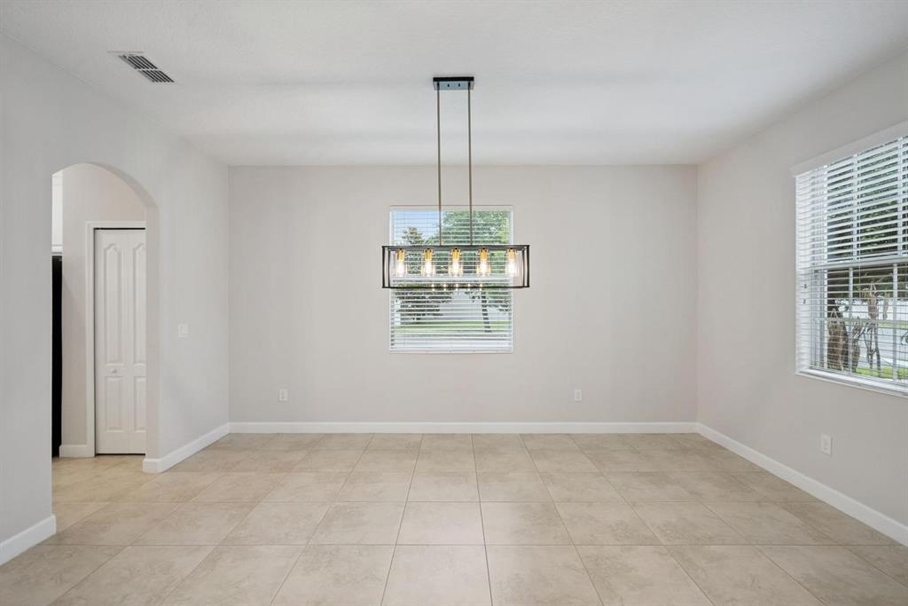 An empty dining room features light tile flooring, a rectangular chandelier, and two windows — 6100 CYPRESS HILL ROAD, WINTER GARDEN, FL