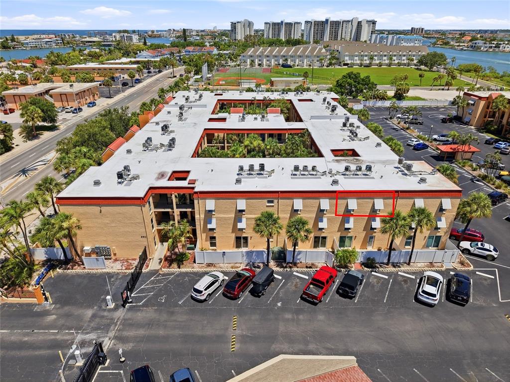 An aerial view shows a multi-story apartment building with a central courtyard and parking — 8911 BLIND PASS ROAD UNIT 302, ST PETE BEACH, FL