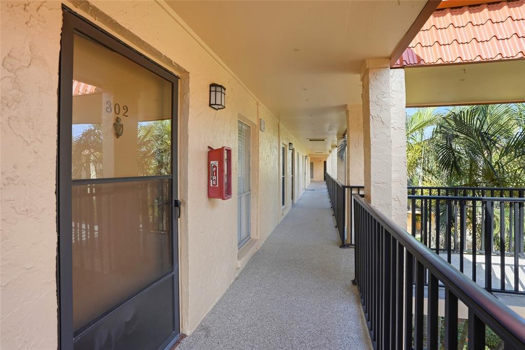 An outdoor apartment hallway features a screen door labeled 302, a fire extinguisher, and railings — 8911 BLIND PASS ROAD UNIT 302, ST PETE BEACH, FL