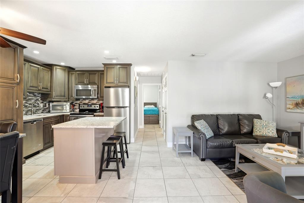 An open-concept kitchen with stainless steel appliances and an island overlooks a living area — 8911 BLIND PASS ROAD UNIT 302, ST PETE BEACH, FL