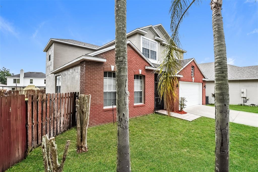 A two-story house with a red brick facade, a garage, and palm trees in the yard — 14401 KRISTENRIGHT LANE, ORLANDO, FL