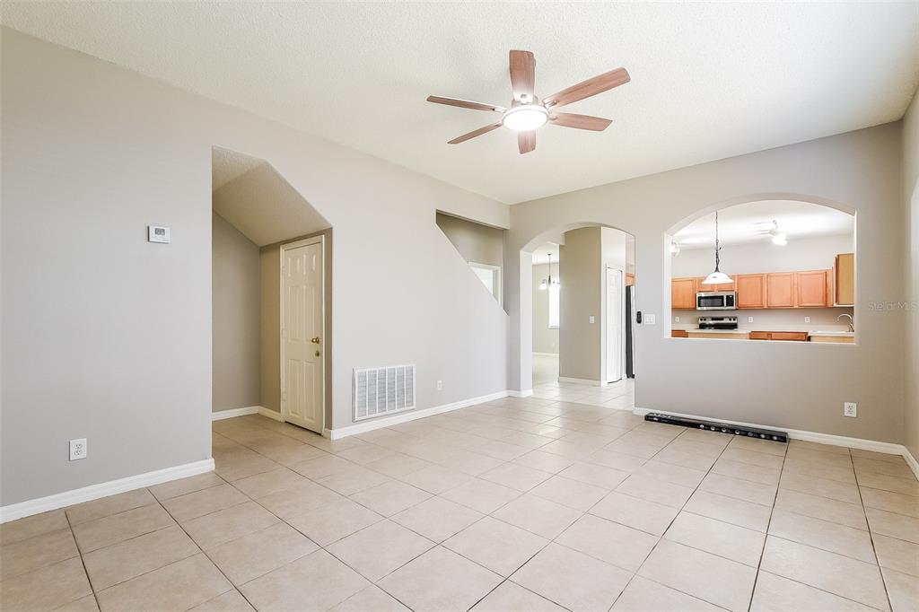 A living room with beige tile floors, a ceiling fan, and an arched kitchen pass-through — 14401 KRISTENRIGHT LANE, ORLANDO, FL