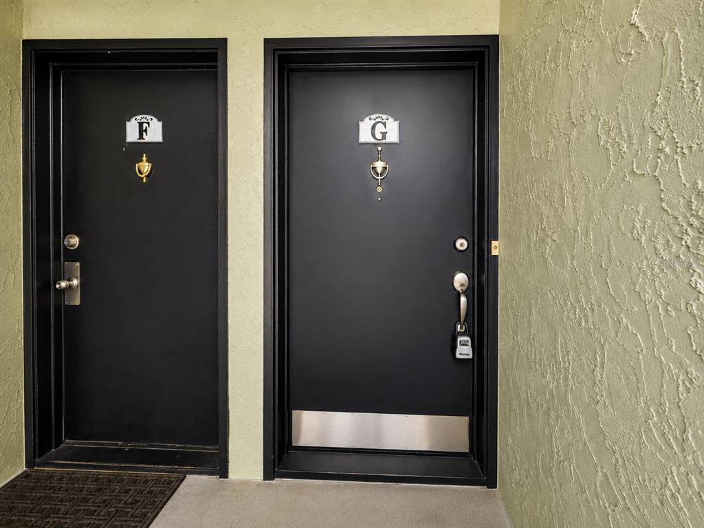 Two black doors labeled F and G are set into a light green textured wall — 940 LAKE DESTINY ROAD UNIT G, ALTAMONTE SPRINGS, FL