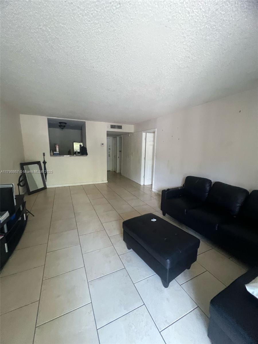 A living room features light-colored tile flooring, white walls, and a black leather sofa set — 482 NW 165th St Rd # A203, Miami FL 33169, MIAMI, FL