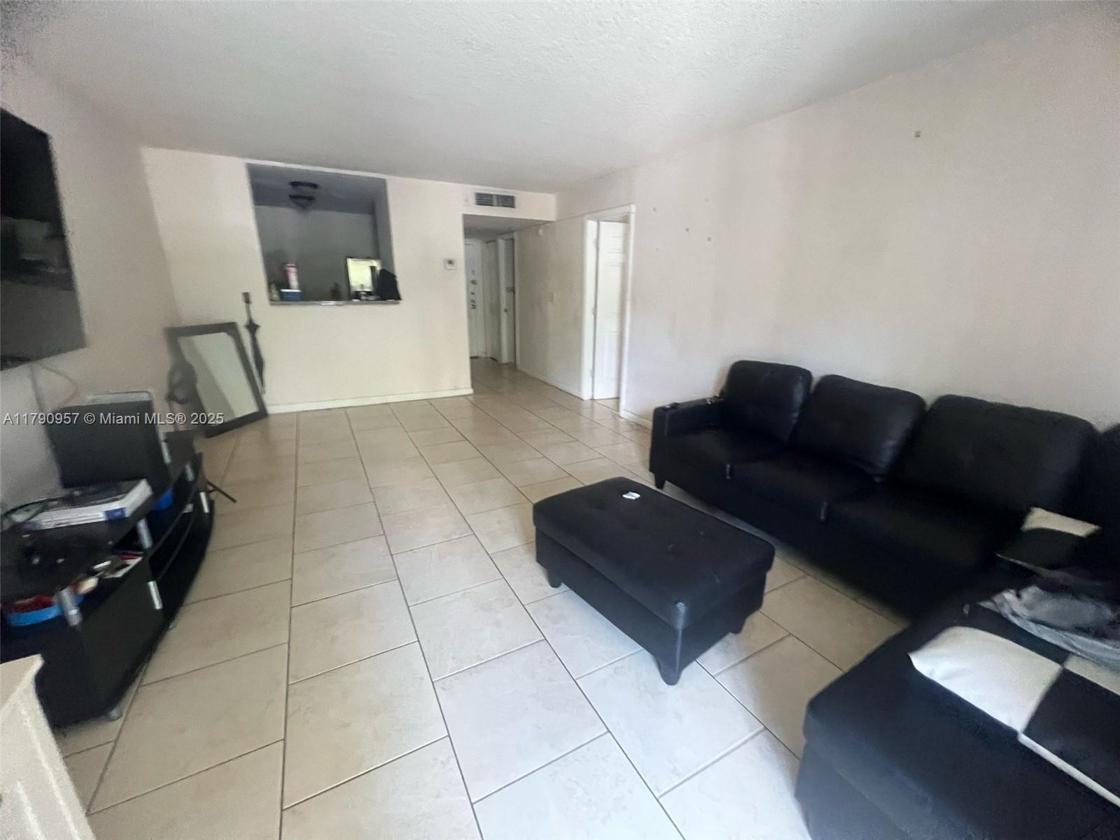 A living room features light tile flooring, white walls, and a black sectional sofa — 482 NW 165th St Rd # A203, Miami FL 33169, MIAMI, FL