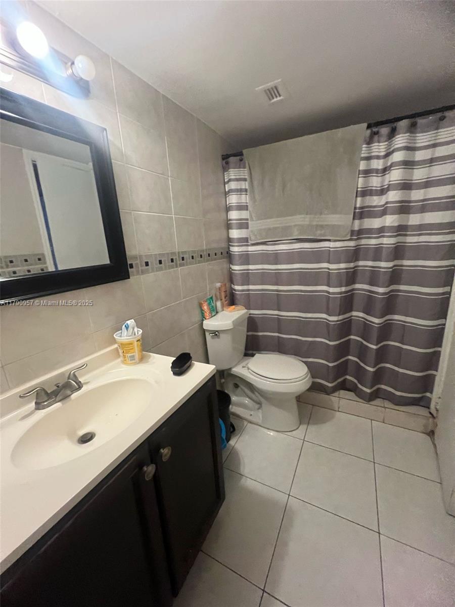 A bathroom features a dark wood vanity, a toilet, and a shower with a striped curtain — 482 NW 165th St Rd # A203, Miami FL 33169, MIAMI, FL