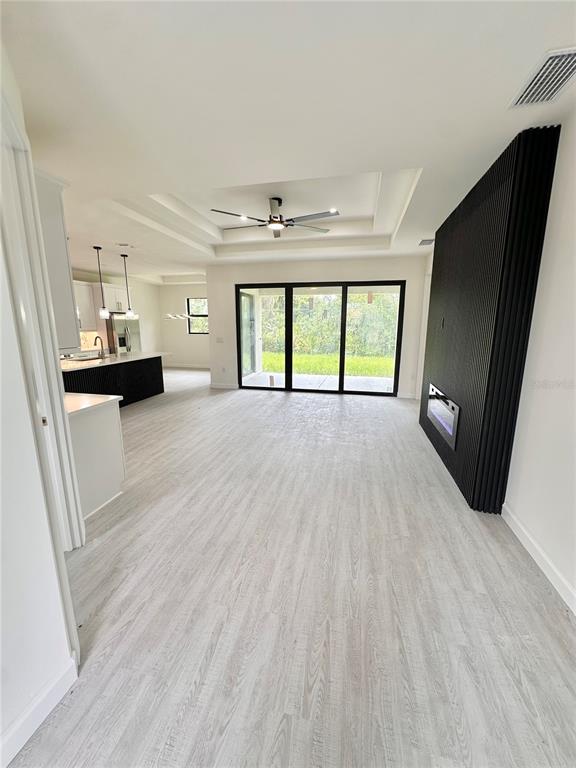 An open-concept living area features light wood-look flooring, a tray ceiling, and a black fireplace — 4653 SAN LUIS TERRACE, NORTH PORT, FL