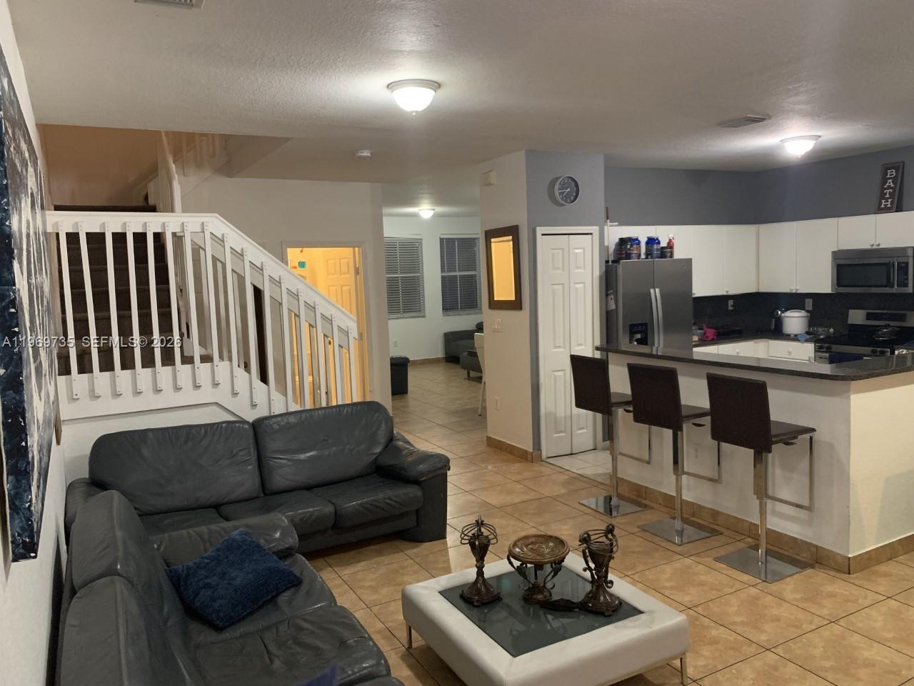 An open-concept living room and kitchen featuring tile floors, a staircase, and bar seating — 6243 SW 165th Ave, Miami FL 33193, MIAMI, FL
