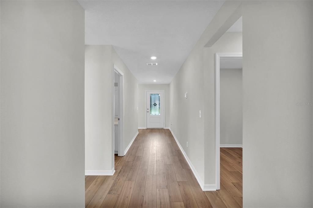 A hallway with light gray walls, wood-look flooring, and a white front door — 34 PRESIDENTIAL LANE, PALM COAST, FL