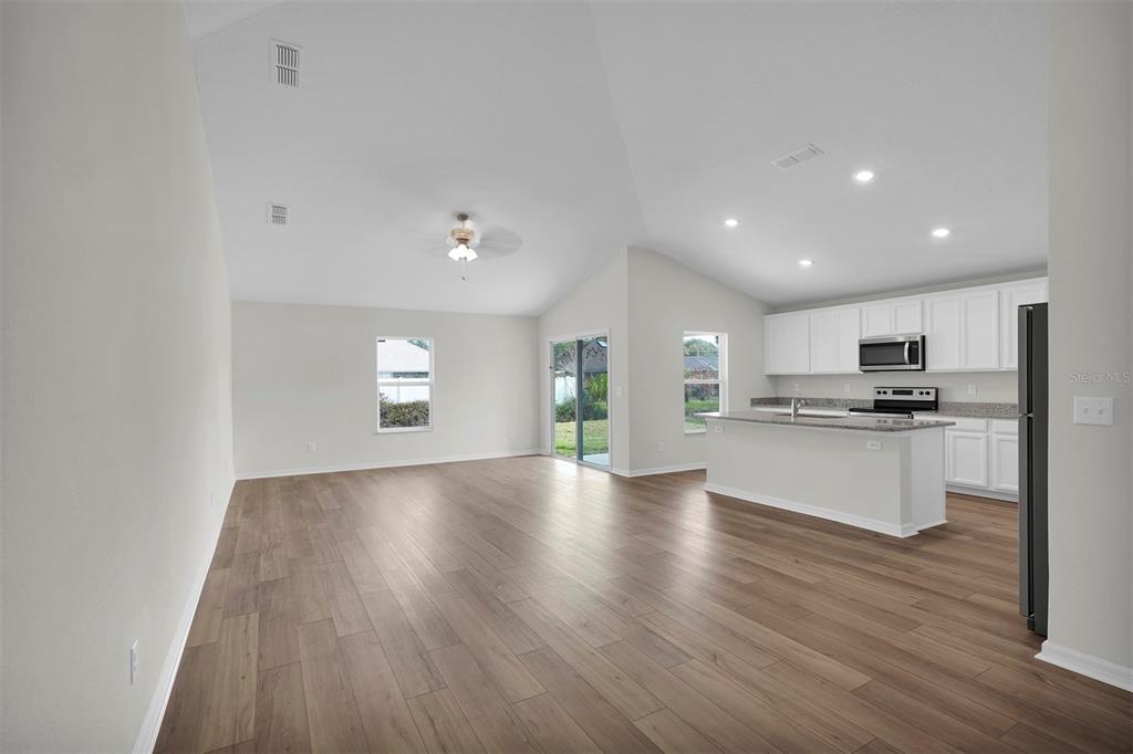 An open-concept living room and kitchen with vaulted ceilings, light wood flooring, and white cabinetry — 34 PRESIDENTIAL LANE, PALM COAST, FL