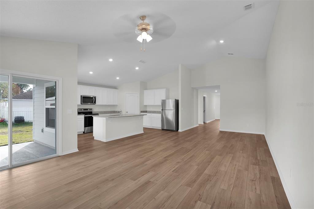 An open-concept kitchen and living area features light wood flooring, white cabinetry, and stainless appliances — 34 PRESIDENTIAL LANE, PALM COAST, FL