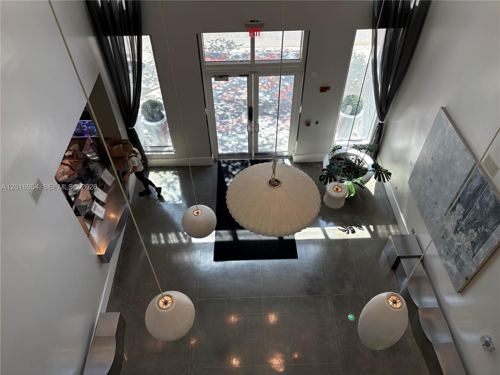 A high-angle view of a modern building lobby featuring large pendant lights and concrete flooring — 133 NE 2nd Ave # 210, Miami FL 33132, MIAMI, FL