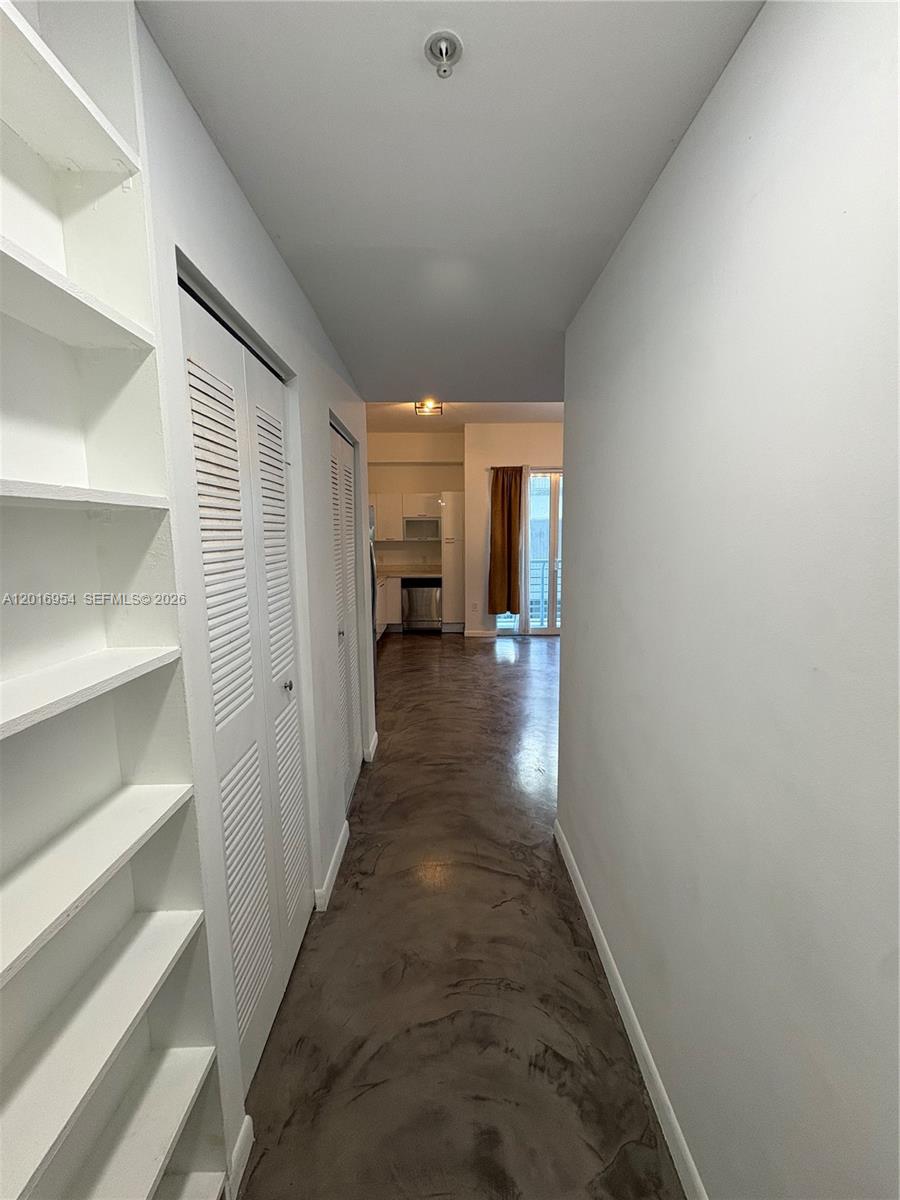 A hallway with white shelving and louvered closet doors leads to an open kitchen area — 133 NE 2nd Ave # 210, Miami FL 33132, MIAMI, FL