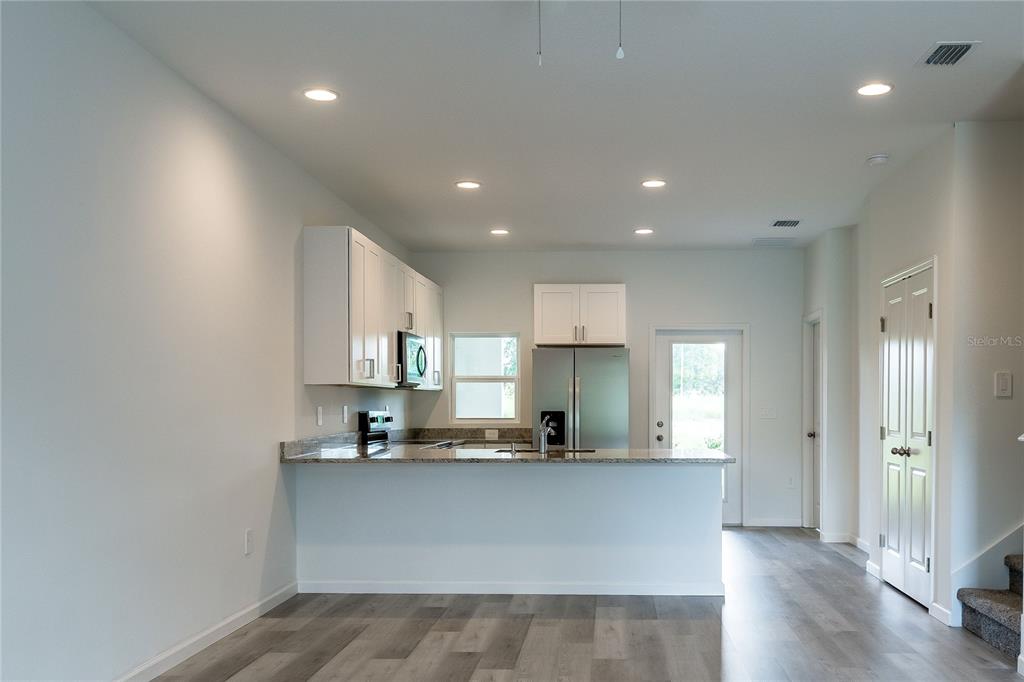 A kitchen features white cabinets, granite countertops, stainless steel appliances, and gray wood-look flooring — 5341 VISTA LAGO DRIVE, ORLANDO, FL