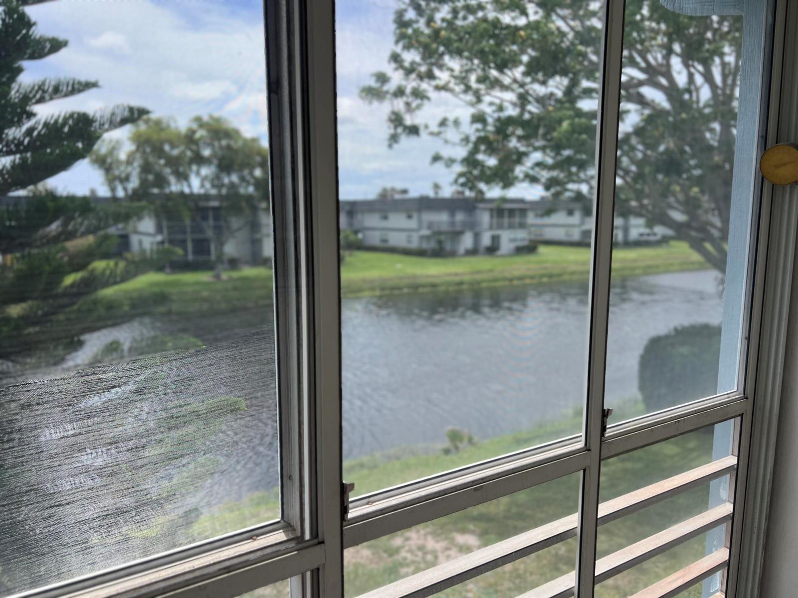 A view of a lake and apartment buildings seen through a screened-in porch window — 424 Saxony, Delray Beach FL 33446, DELRAY BEACH, FL