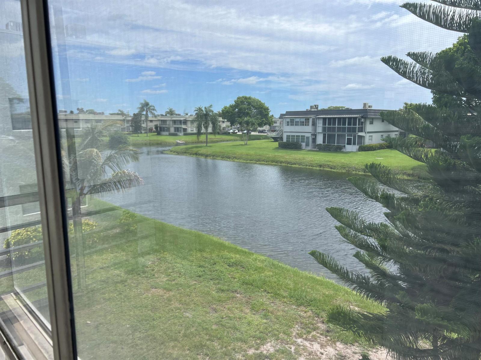 A view of a lake and apartment buildings seen through a window screen — 424 Saxony, Delray Beach FL 33446, DELRAY BEACH, FL