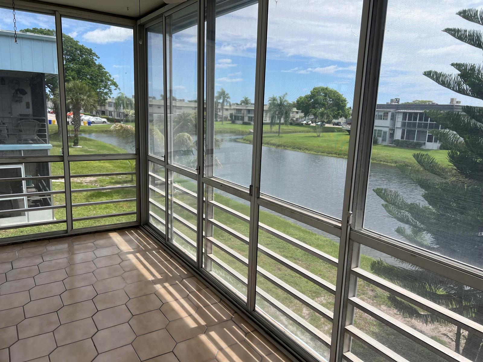 A screened-in porch with hexagonal tile flooring overlooks a canal and residential buildings — 424 Saxony, Delray Beach FL 33446, DELRAY BEACH, FL