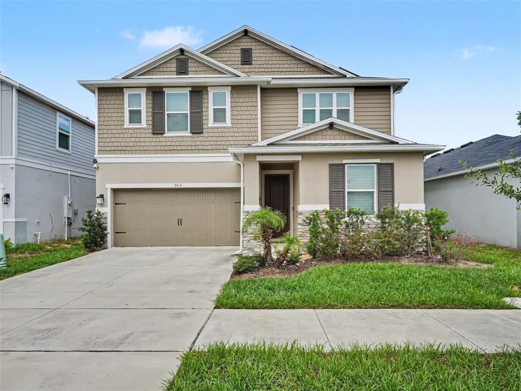A two-story suburban house features a tan stucco and shingle exterior with a two-car garage — 905 OVERPOOL AVENUE, DAVENPORT, FL
