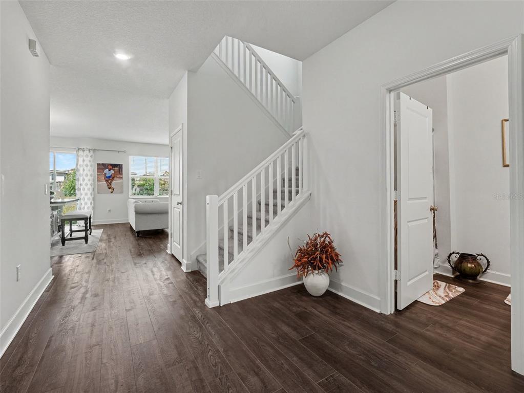 An entryway with dark wood-look flooring, a white staircase, and an open living area beyond — 905 OVERPOOL AVENUE, DAVENPORT, FL