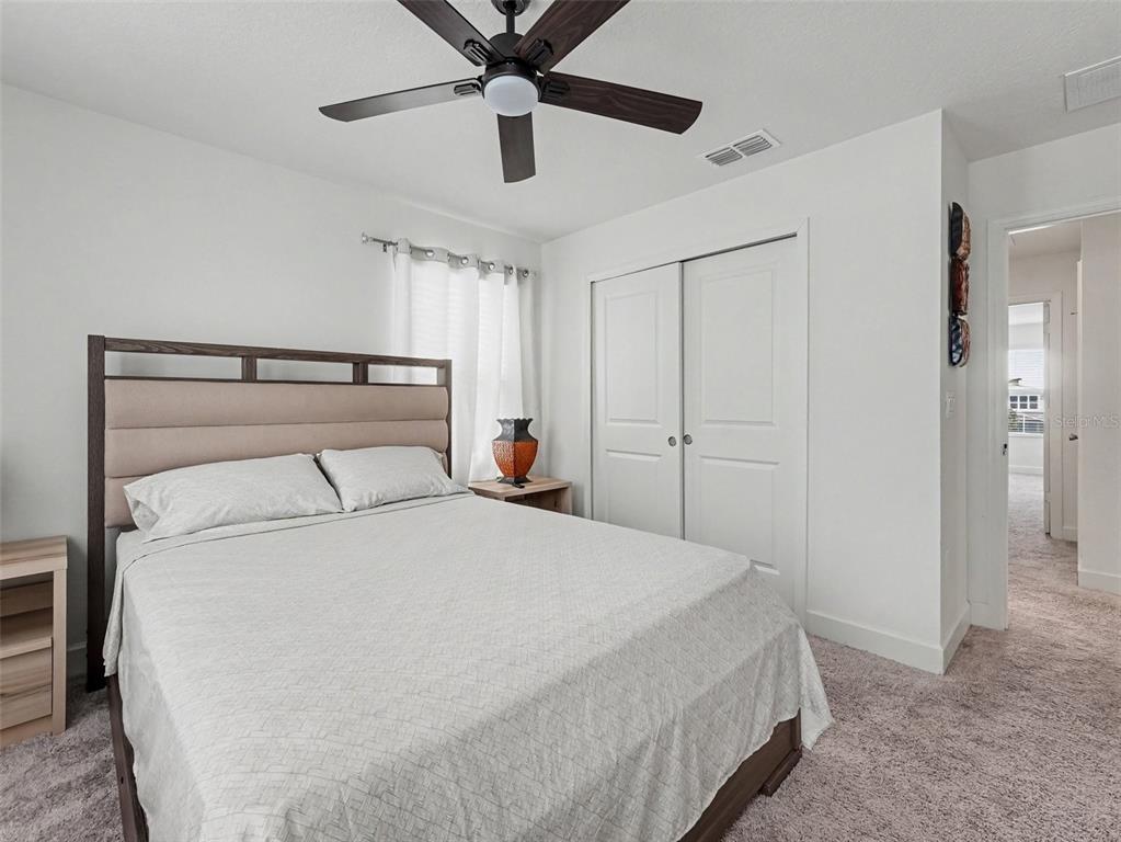 A bedroom features a bed with a tan headboard, white bedding, and a ceiling fan — 905 OVERPOOL AVENUE, DAVENPORT, FL