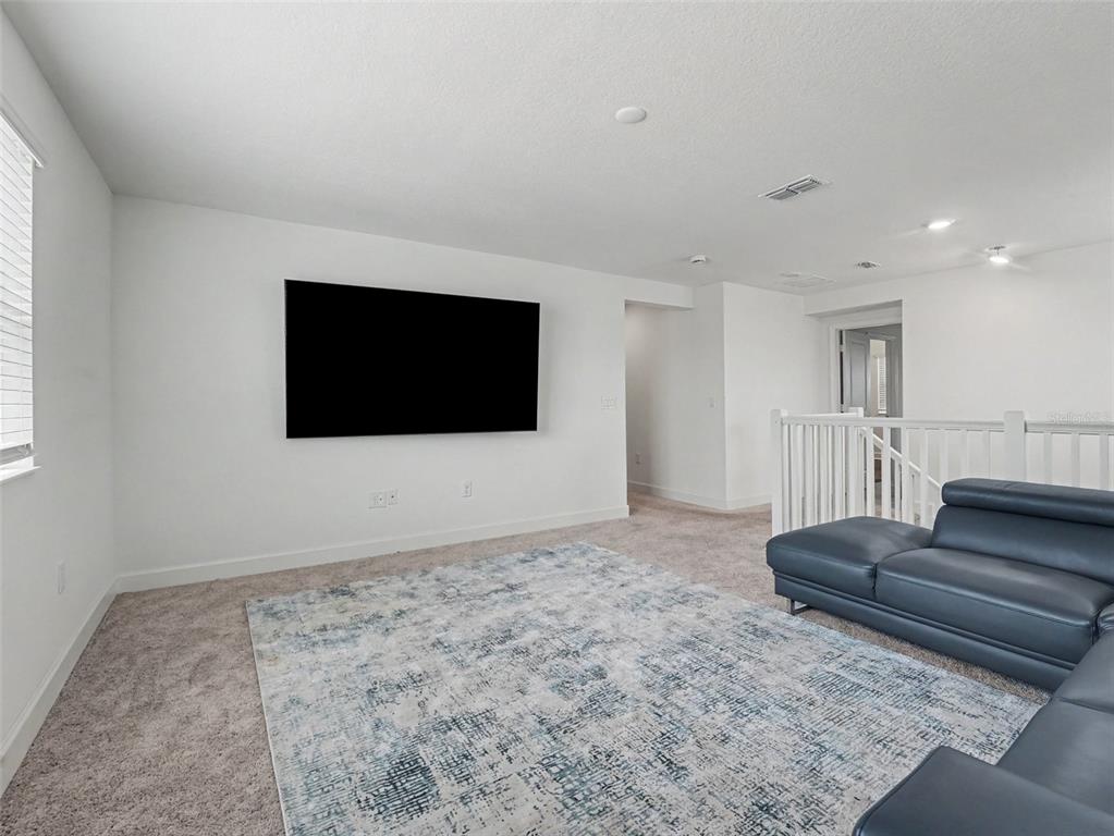 A carpeted living room features a wall-mounted television, a blue sectional sofa, and white walls — 905 OVERPOOL AVENUE, DAVENPORT, FL