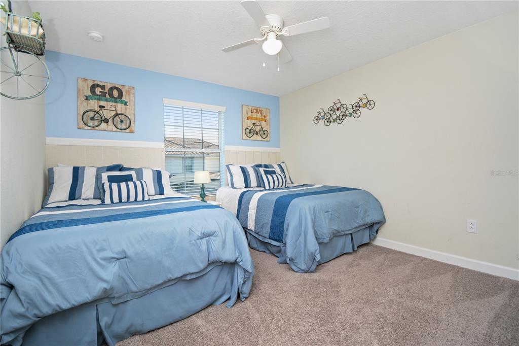 A bedroom features two beds with blue bedding, light blue and beige walls, and bicycle decor — 3079 TOM SAWYER DRIVE, KISSIMMEE, FL