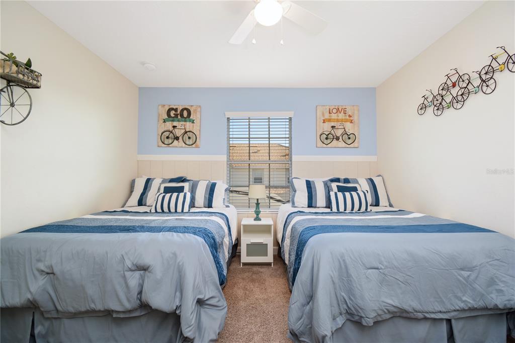 A bedroom features two beds with blue bedding, a central nightstand, and bicycle-themed wall decor — 3079 TOM SAWYER DRIVE, KISSIMMEE, FL