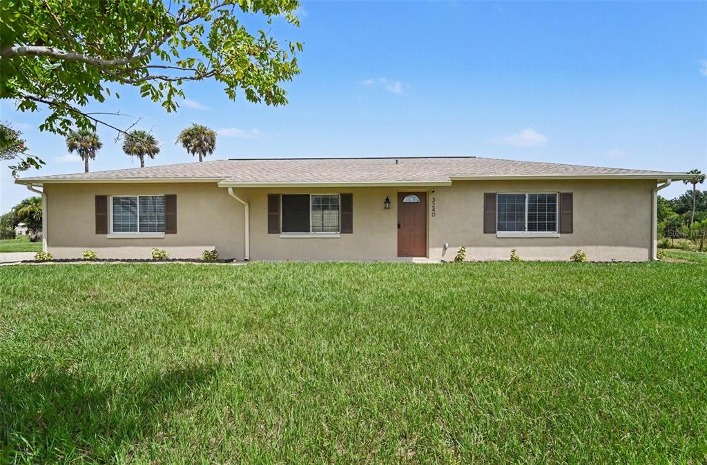 A single-story house with a tan exterior, brown shutters, and a front door sits on grass — 3240 CORAL AVENUE, MIMS, FL
