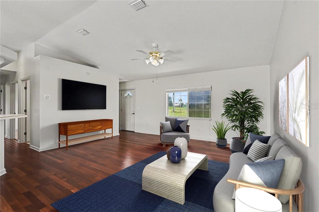 A living room features dark wood flooring, a mounted television, a ceiling fan, and furniture — 3240 CORAL AVENUE, MIMS, FL