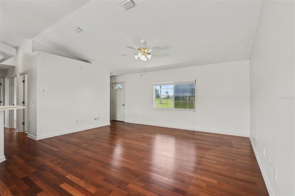 An empty living room with hardwood floors, white walls, a ceiling fan, and a window — 3240 CORAL AVENUE, MIMS, FL