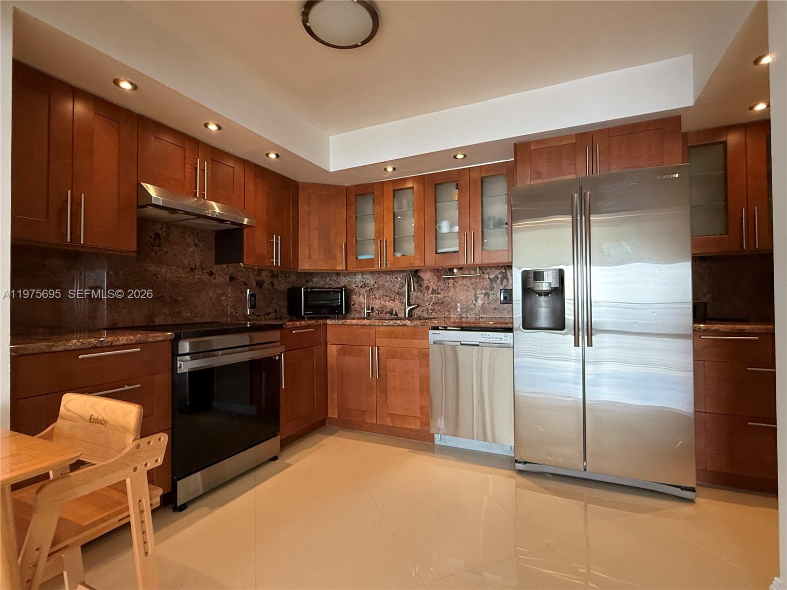 A kitchen features wood cabinets, stainless steel appliances, and a dark stone backsplash — 2101 S Ocean Dr # 1201, Hollywood FL 33019, HOLLYWOOD, FL