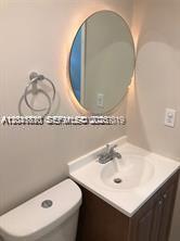 A bathroom features a vanity with a white sink, a round backlit mirror, and a toilet — 1575 NW 127th St, North Miami FL 33167, NORTH MIAMI, FL