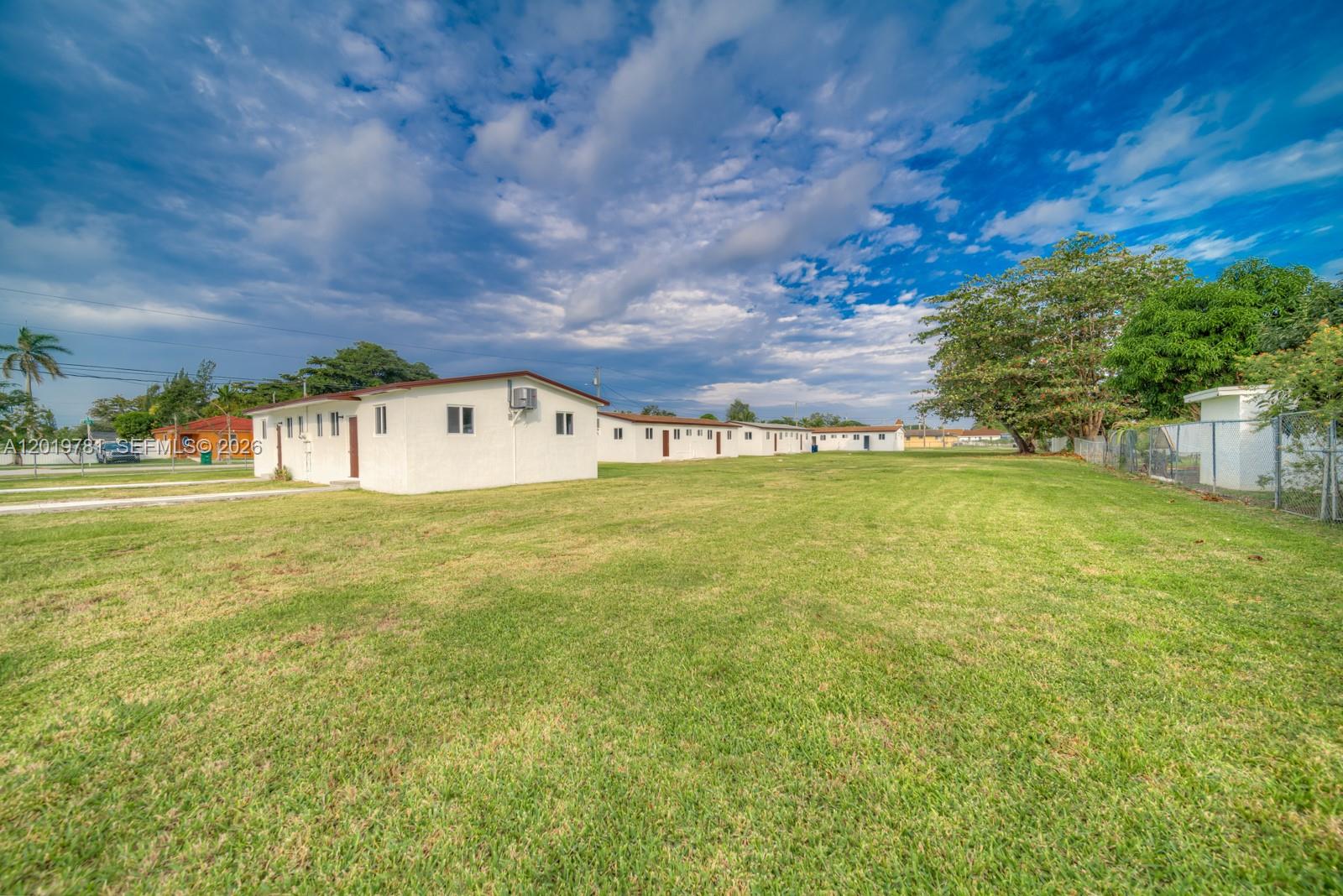 A long, white, single-story residential building sits on a large, grassy lot under a cloudy sky — 17727 SW 103rd Ave # 17727, Miami FL 33157, MIAMI, FL