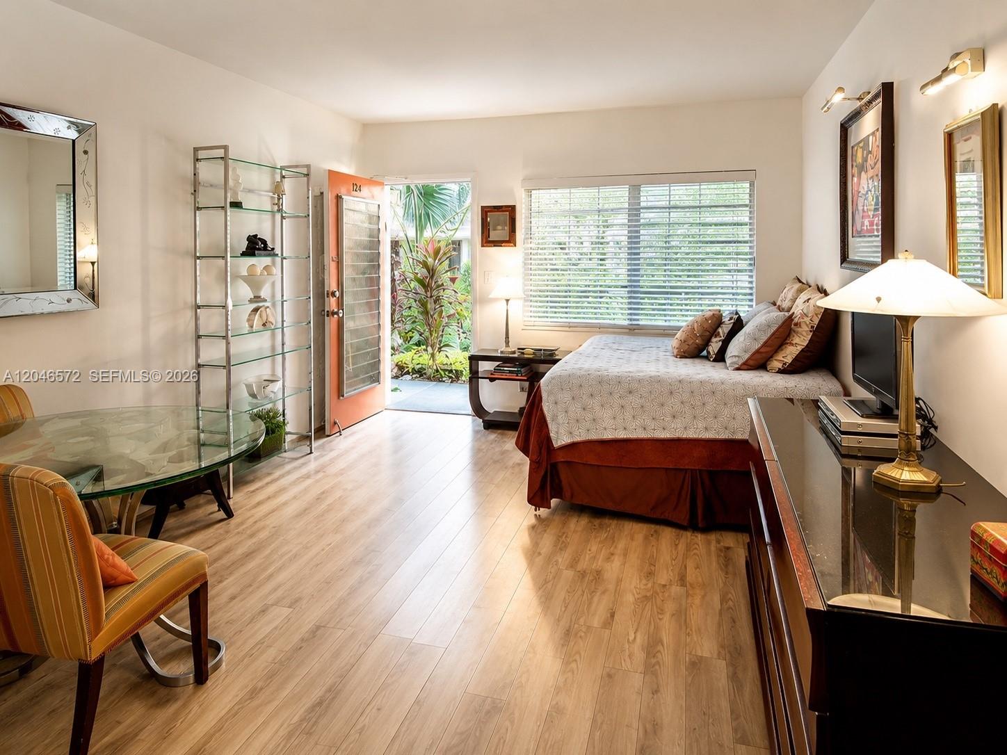 A studio apartment features a bed, dining area, glass shelving, and an open exterior door — 1050 Pennsylvania Ave # A, Miami Beach FL 33139, MIAMI BEACH, FL